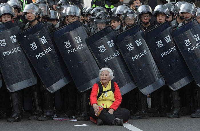 Пожилая женщина сидит перед полицейскими, пытаясь таким образом защитить участников мощной антиправительственной акции протеста.