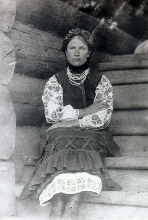 Женщина в традиционном украинском костюме, сидящая на ступеньке крыльца.  