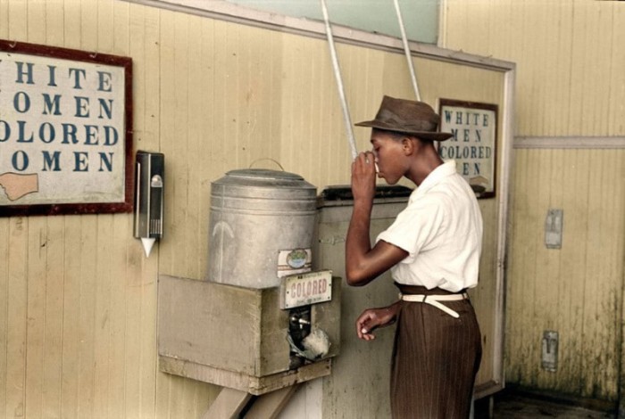 Афроамериканец пьет из автомата для питьевой воды.