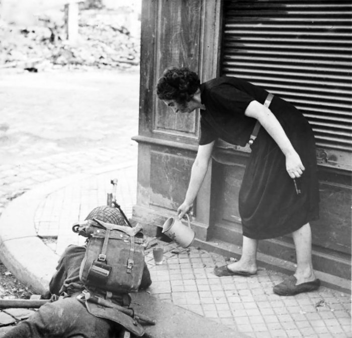 Женщина наливает чай британскому солдату во время уличного боя после высадки союзников в Нормандии в 1944 году.