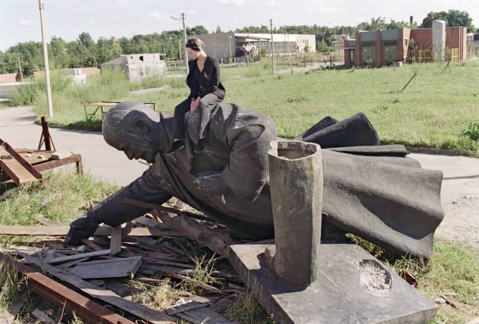 Молодая девушка сидит на сброшенной статуе Ленина в Вильнюсе.