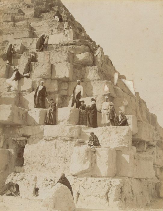 Европейские туристы и местные гиды поднимаются на одну из пирамид в Гизе.