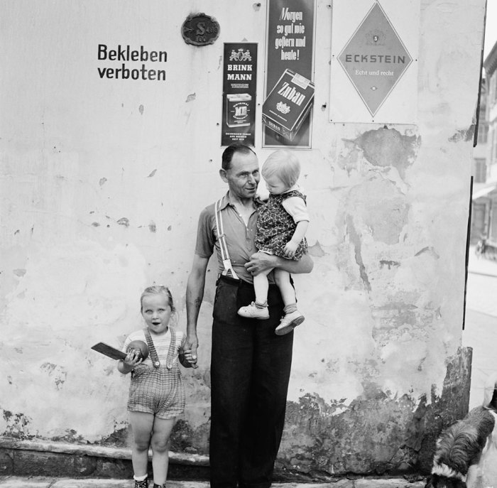 Отец с двумя детьми возле стенки, на которой вопреки запрету висят рекламные плакаты. Германия, 1955 год.