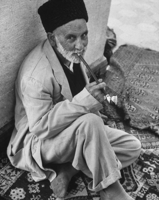 Пожилой мусульманин курящий, сидя на коврике.