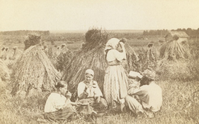 Три женщины и мужчина обедают на пшеничном поле.