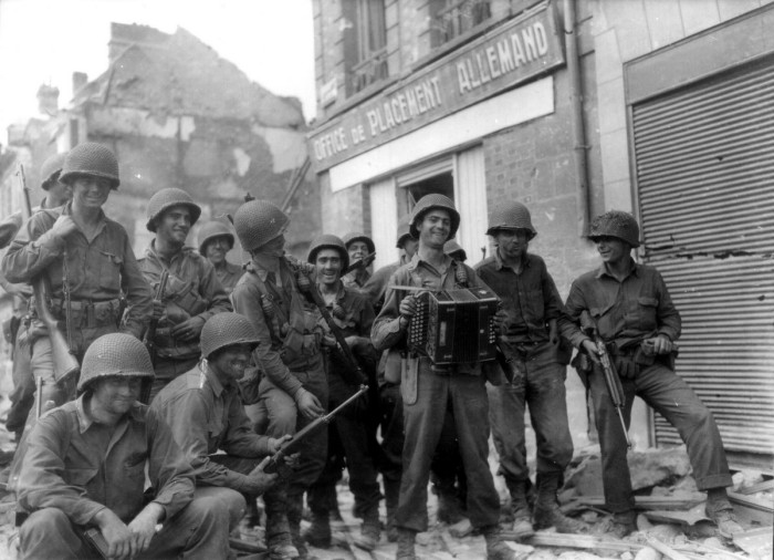 Группа солдат с аккордеоном рядом с разрушенным немецким пунктом сбора людей для принудительных работ.