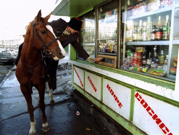 Казак на лошади покупает водку в киоске после парада в Москве.