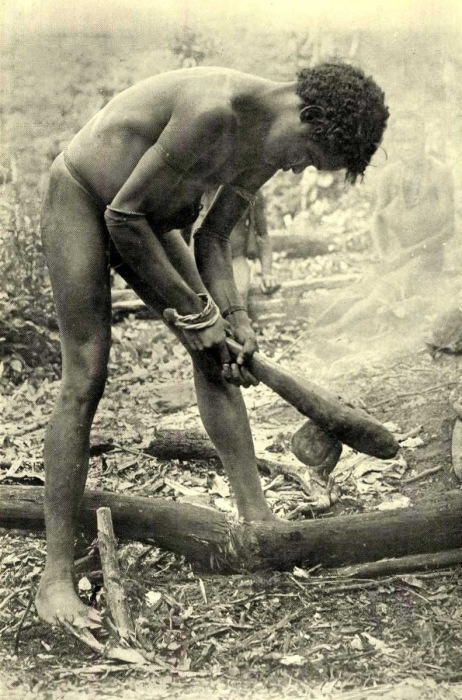 Молодой человек рубит ствол каменным топором.