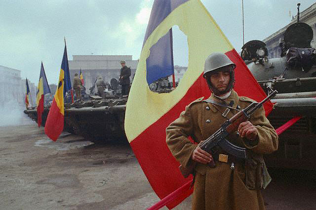 Румынский солдат на фоне флага с вырезанным гербом. | Фото: gazeta.ru.