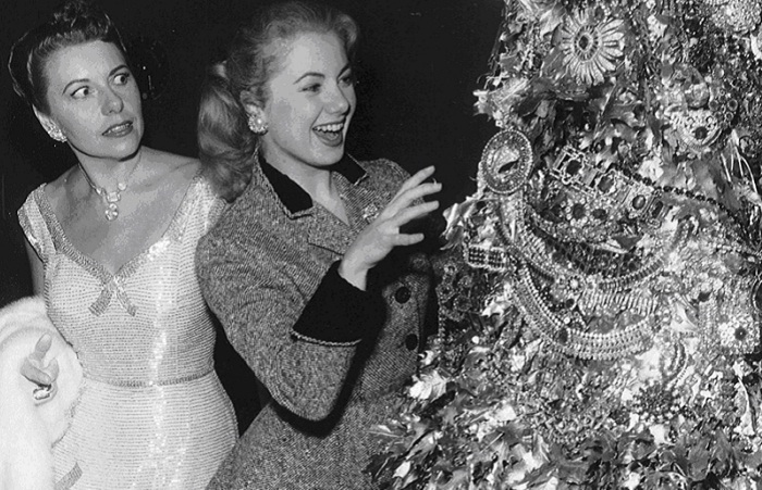 Джоан Касл с ужасом смотрит на Ширли Джонс, которая пытается потрогать ошеломляющую рождественскую елку, сделанную из драгоценностей Джозефа