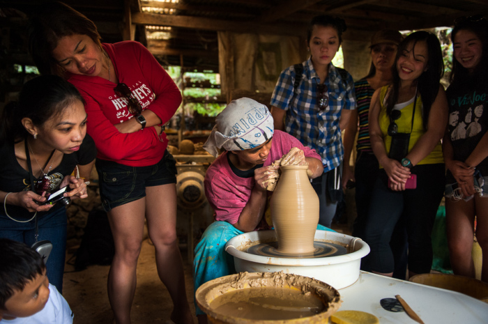 Туристы из Манилы смотрят, как местный житель Сигрид лепит глиняный кувшин.