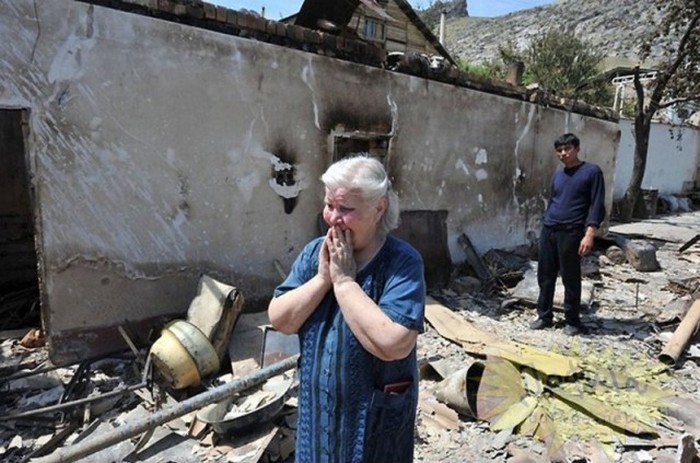 Женщина плачет у своего сгоревшего дома.