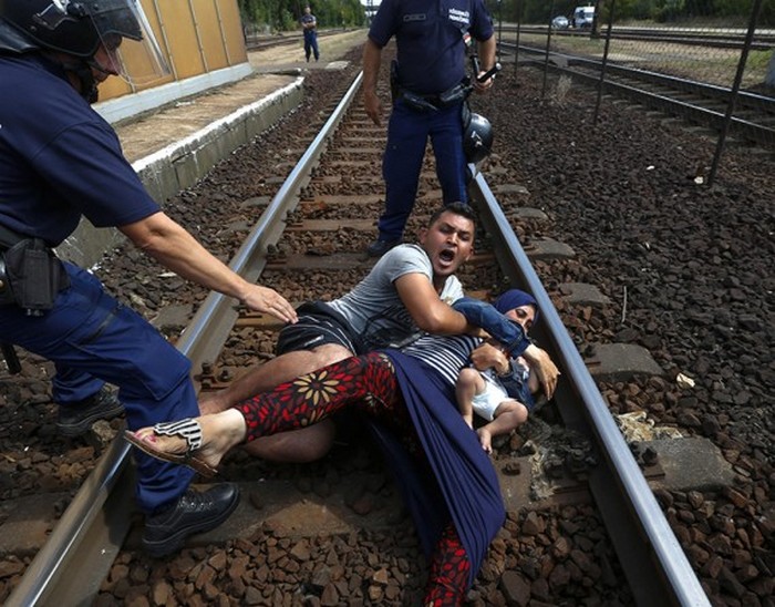 Венгерские полицейские стоят над семьей, которая бросилась на рельсы во время задержания на железнодорожном вокзале в городе Бичке. (Thomson Reuters / Ласло Балог - 3 сентября 2015)