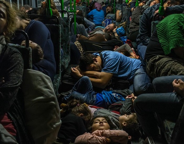 Ахмад Маджид (в синей футболке в центре) спит в проходе автобуса со своими детьми. Справа в зеленом свитере его брат Фарид Маджид, а также другие члены их семьи и десятки других беженцев. Фото сделано в автобусе, выехавшем из Будапешта в Вену. (The New York Times / Маурисио Лима - 5 сентября 2015)