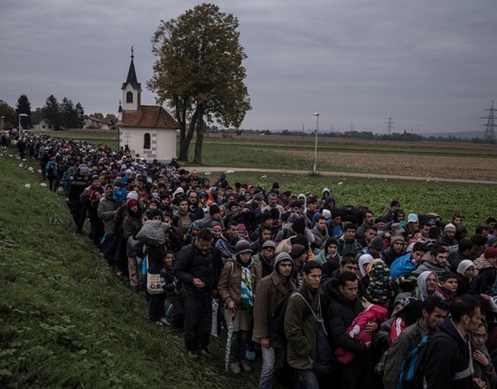 Мигранты в сопровождении словенской полиции проходят мимо церкви, направляясь в регистрационный лагерь на окраине словенского городка Добова.  (The New York Times / Сергей Пономарев - 22 октября 2015)